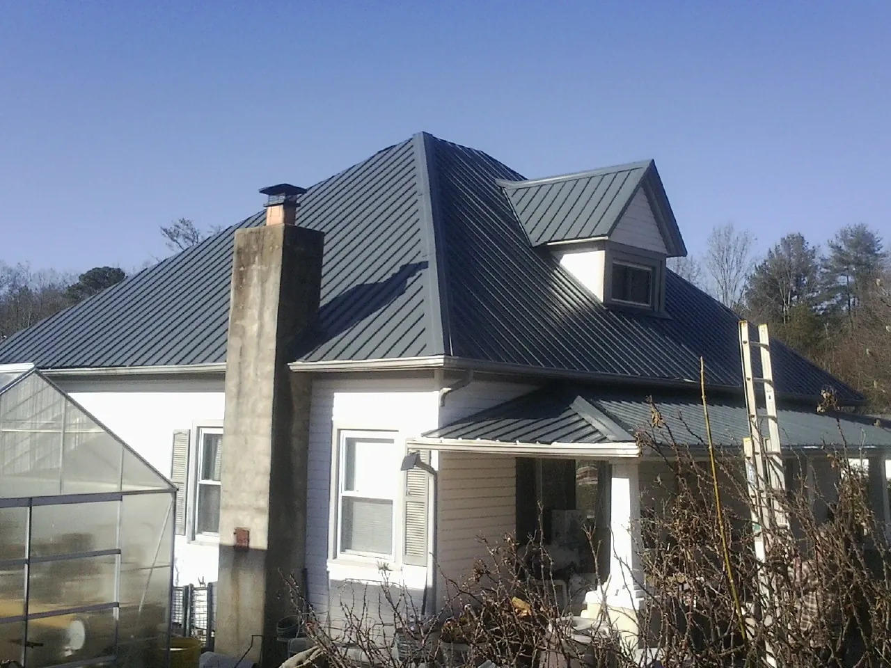 Dark blue standing seam metal roof on a white farmhouse with dormer — Slate & Tile Roof Repair by Roofing Brothers in Millwood