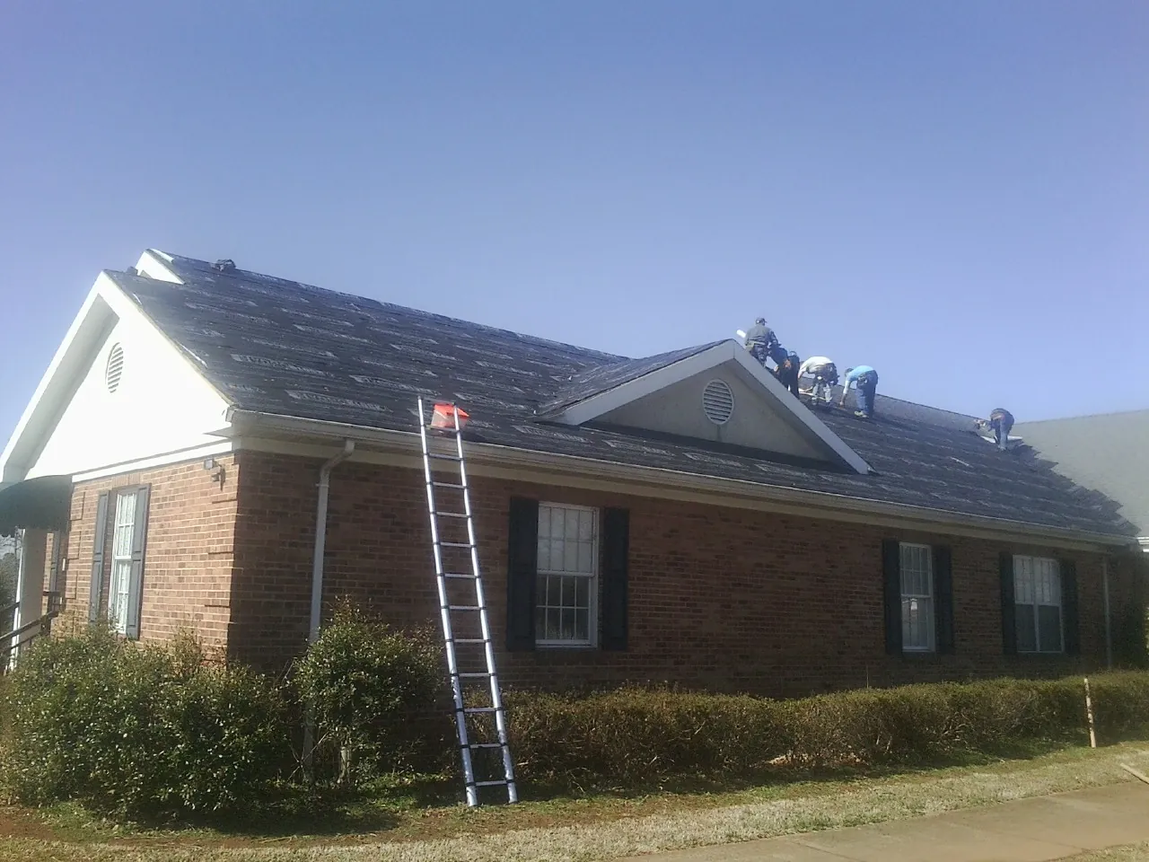 Crew tearing shingles off a brick ranch roof with a ladder set — Metal Roof Repair work by our crew in Millwood