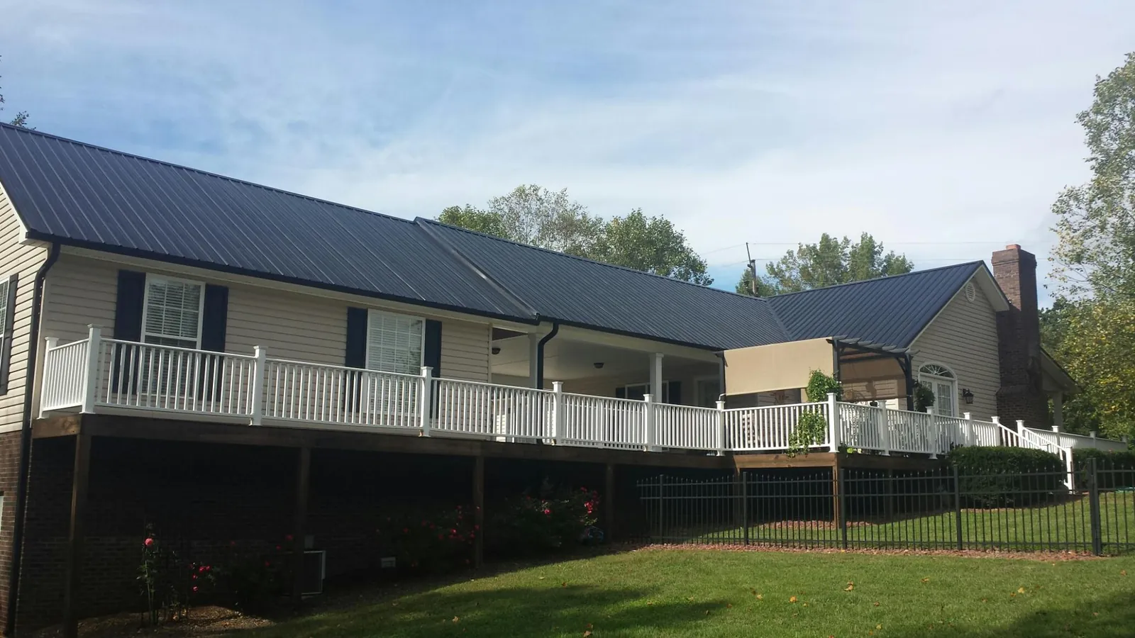 Black metal roof above a long white railed deck on a hillside home in Millwood