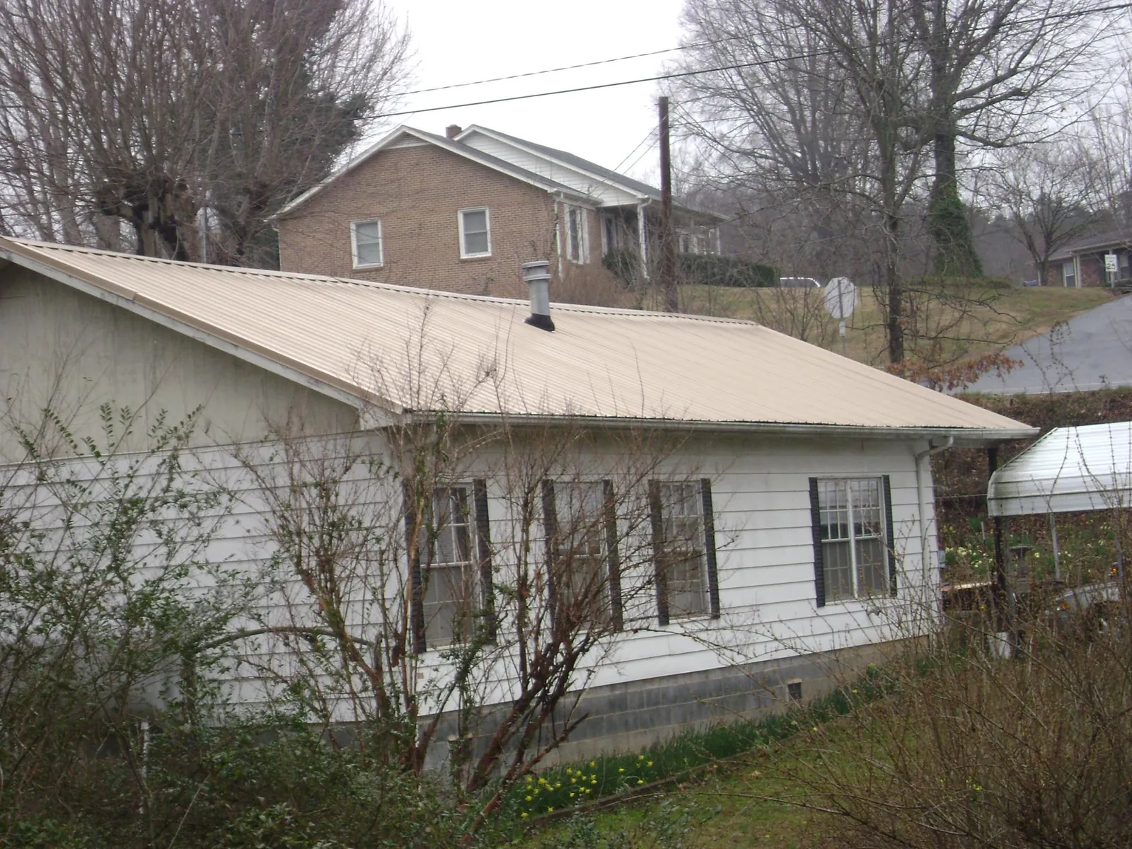Tan metal roof on a white sided house set into a hillside — Commercial Roofing by Roofing Brothers in Millwood